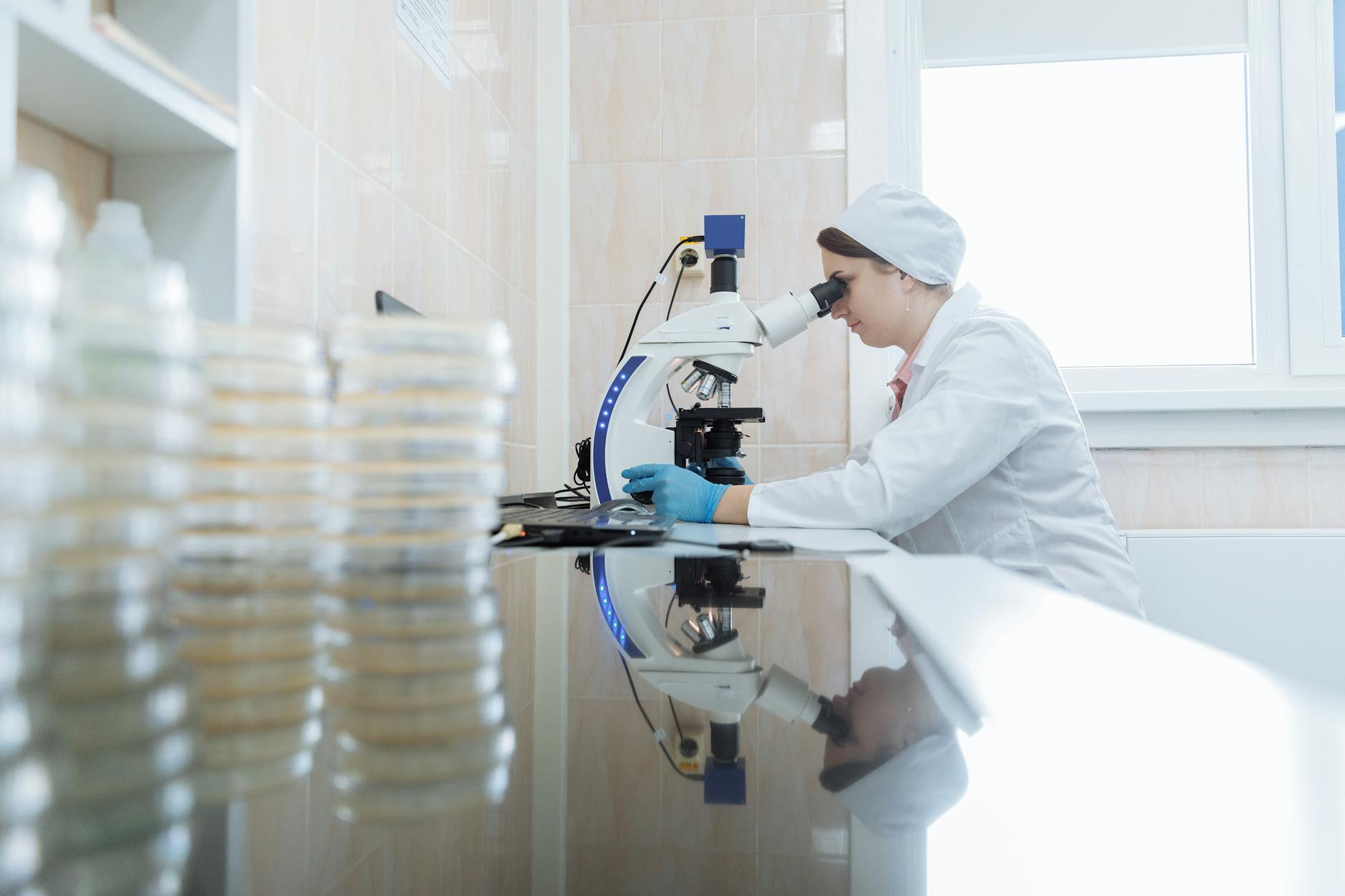 A scientist in a lab coat examining petri dishes under a microscope, with complex molecular diagrams in the background.