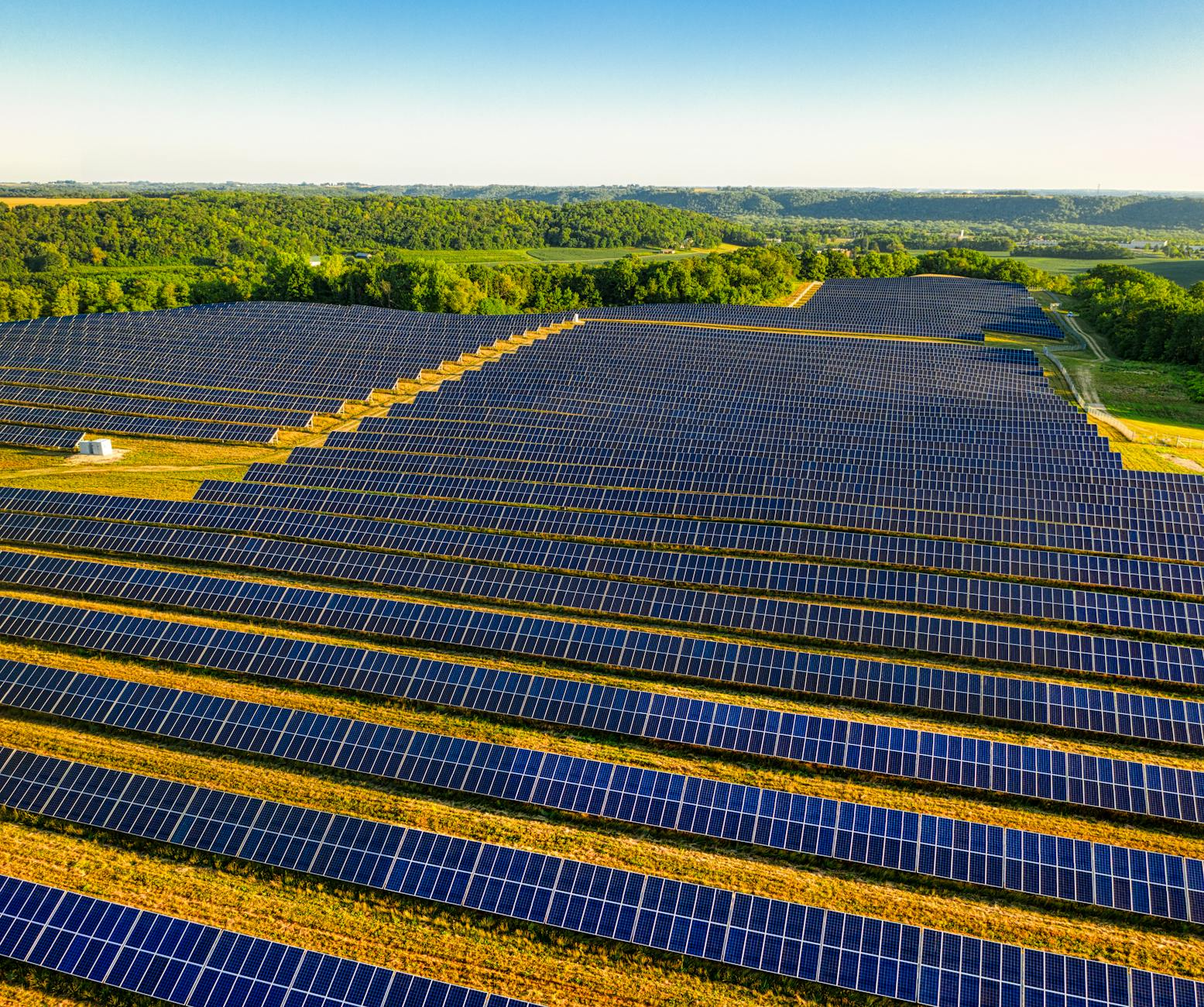 A satellite view of a vast, modern energy landscape, showcasing a large solar farm connected to a grid-scale LDES facility, with transmission lines extending across the terrain.