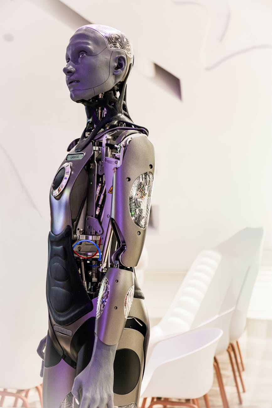 A sleek, futuristic humanoid robot with glowing blue accents is shown in a highly organized, modern warehouse, extending a robotic arm to pick up a package.