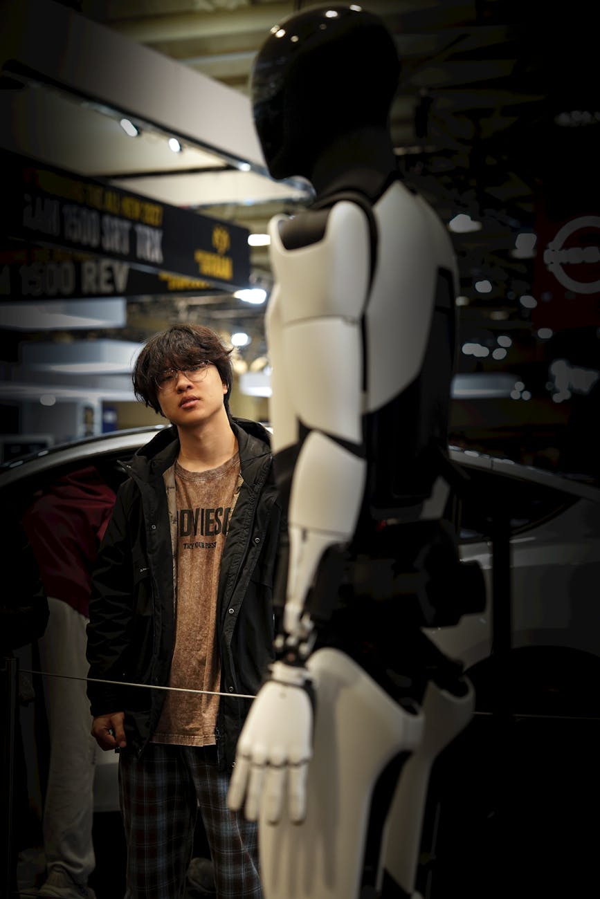 A sleek, futuristic humanoid robot with glowing blue accents, standing in a bustling, modern logistics warehouse, observing a conveyor belt with a discerning gaze.