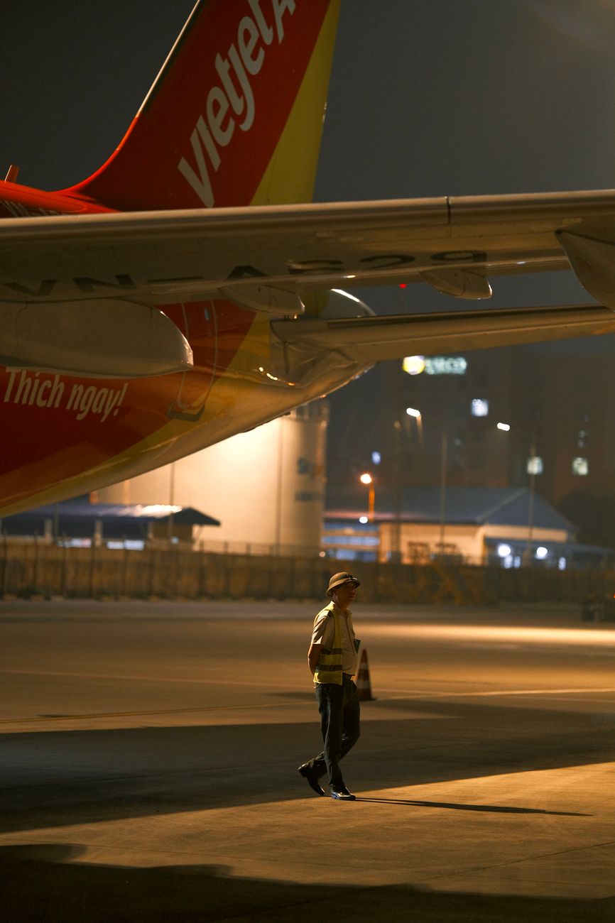 A bustling, futuristic airport hub bathed in warm, sustainable lighting. Electric autonomous vehicles move cargo, while sleek, hydrogen-powered aircraft are being serviced at dedicated refueling stations. The architecture is green and integrated with natural elements.